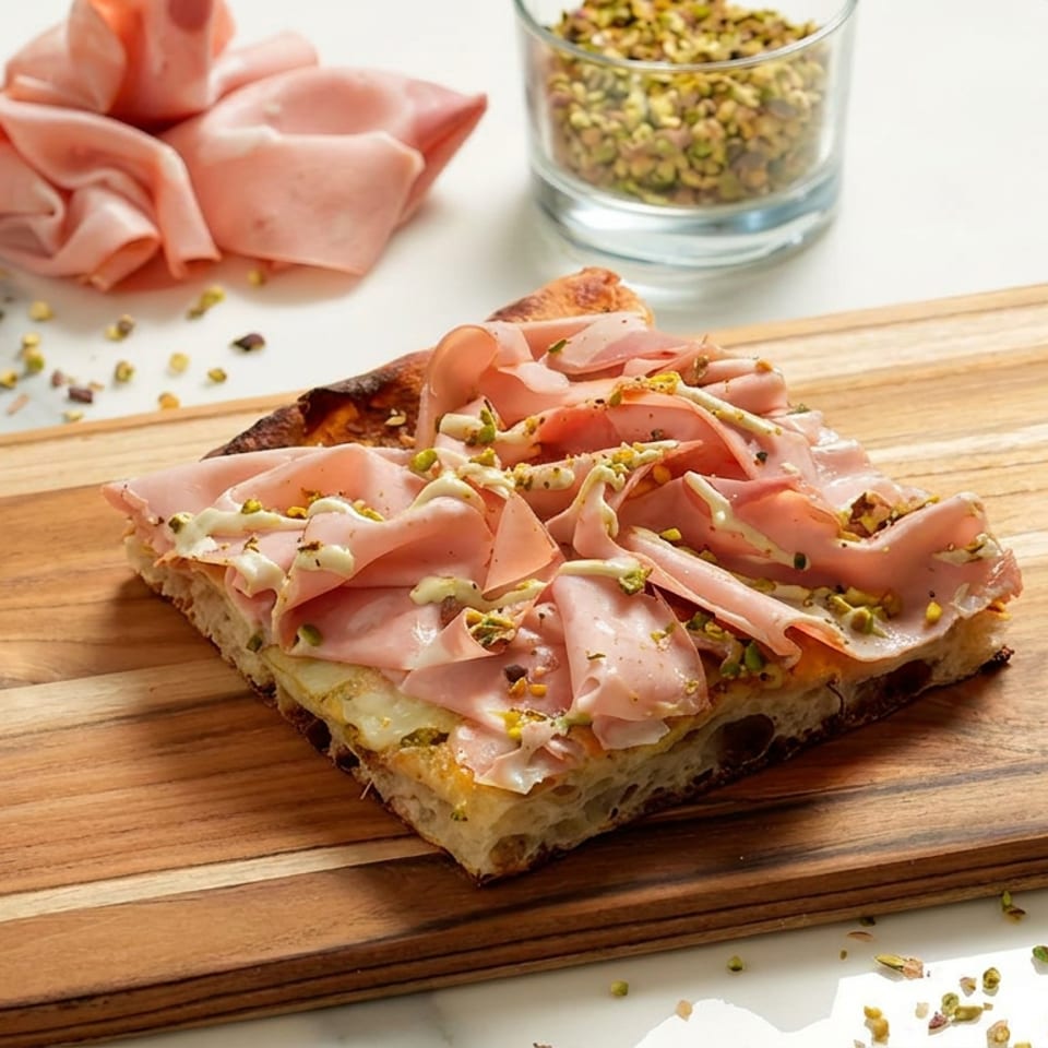 Thick toasted sandwich topped with folded mortadella, creamy cheese, and crushed pistachios on a wooden serving board.
