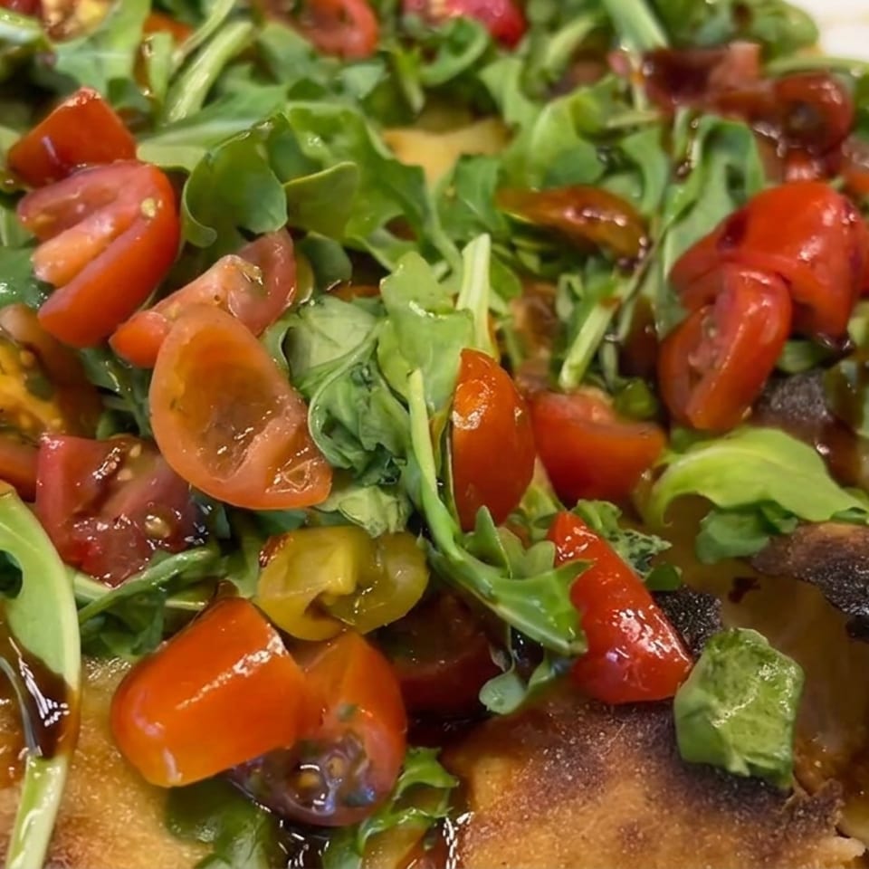 Crispy flatbread topped with arugula, colorful cherry tomatoes, and glossy balsamic drizzle.