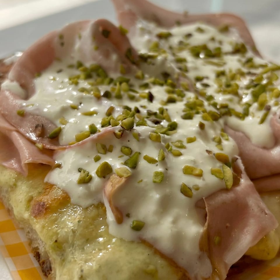 Pistachio-topped pastry layered with creamy white sauce and folded slices of ham on a yellow-checkered plate.
