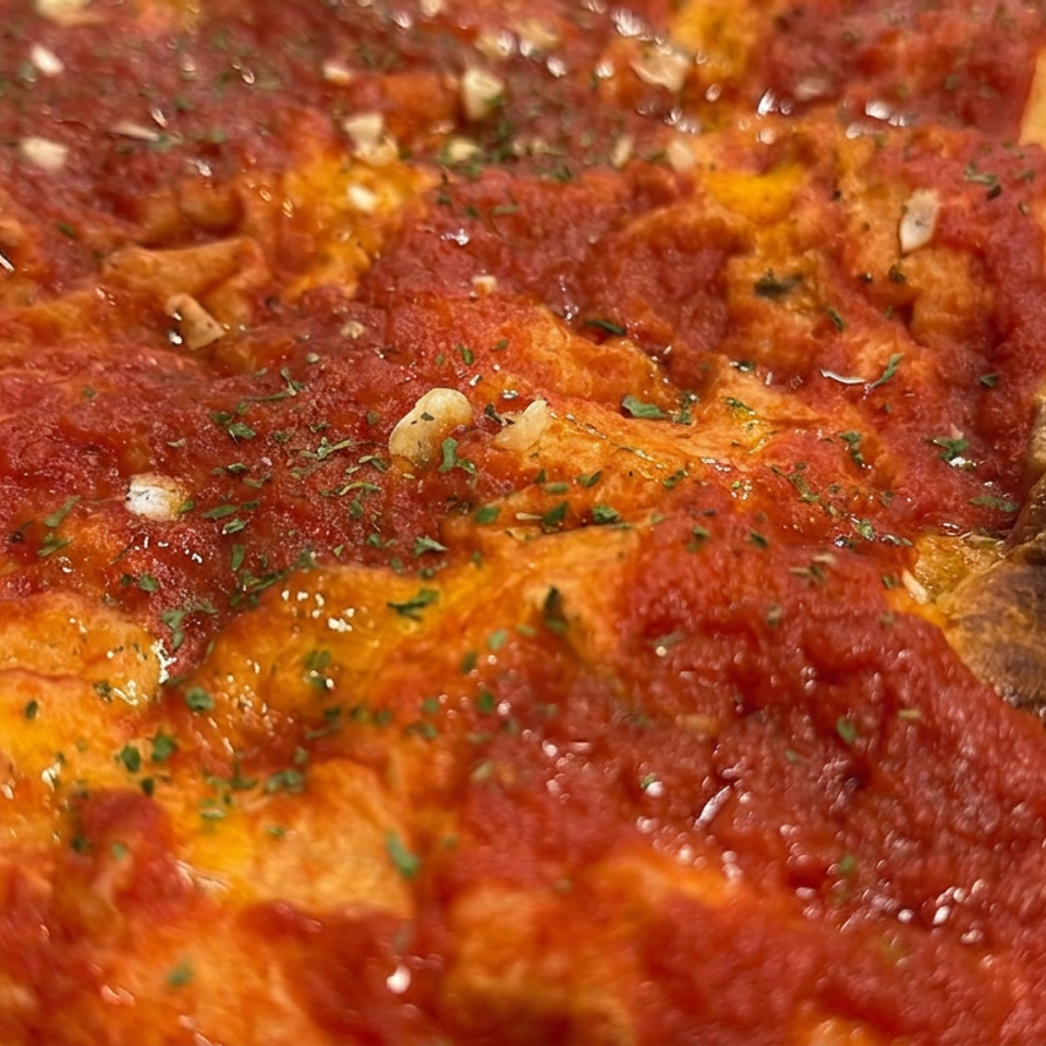 Close-up of a saucy cheese pizza topped with herbs and pepperoni, featuring a thick charred crust.